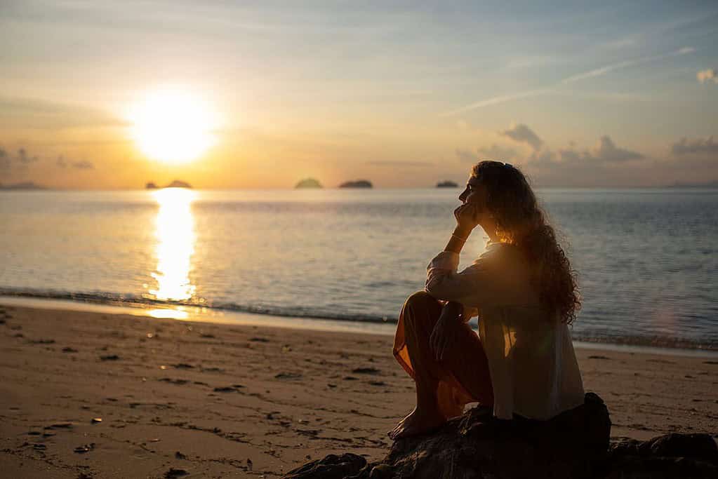 woman on a beach at sunset, setting her realistic goals deep in thought