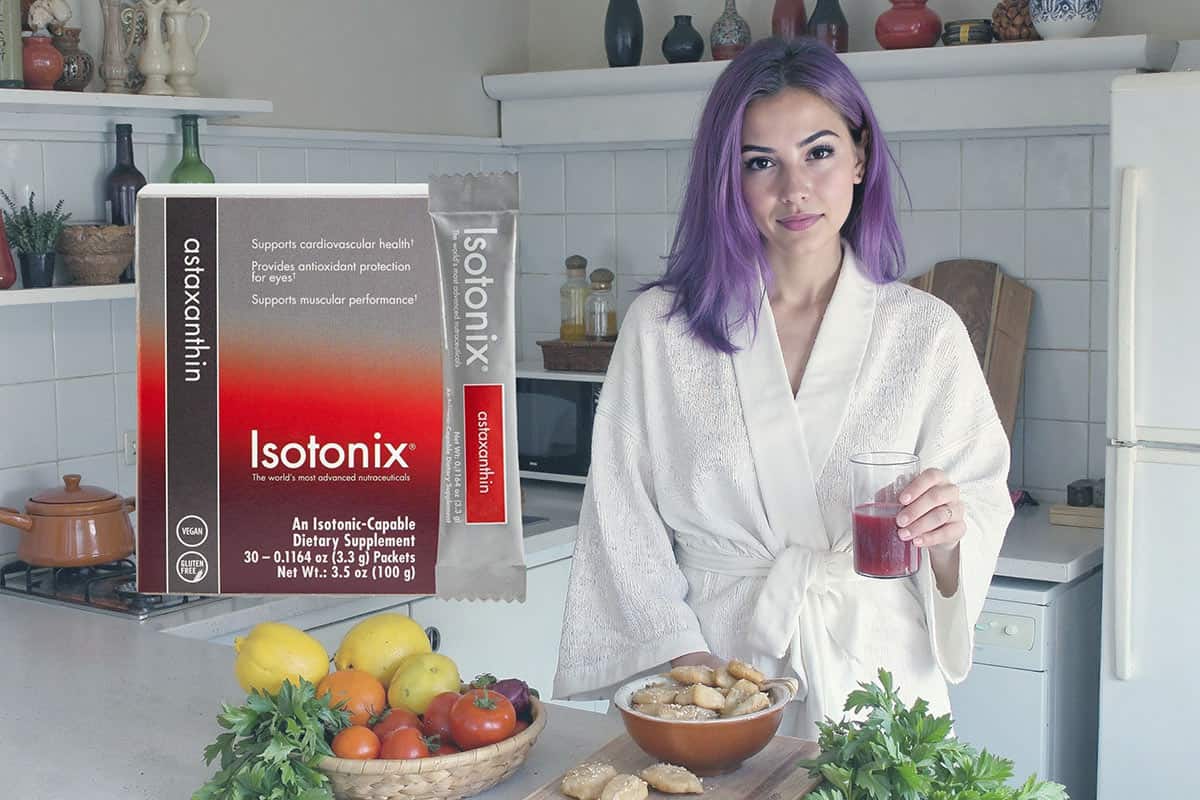 A woman named lyra kade standing in her kitchen drinking a red supplement